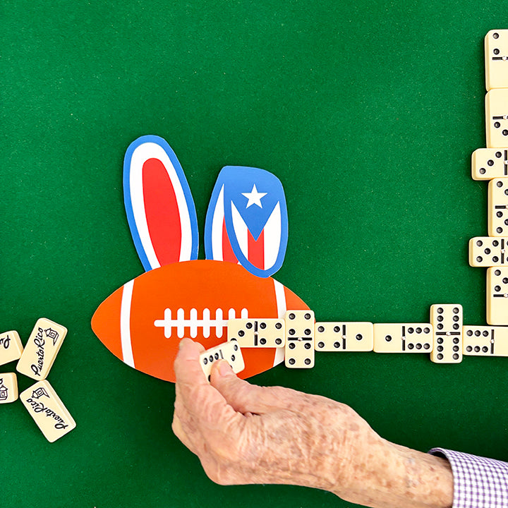 Hand playing with dominoes shaped like a football with Puerto Rican flag design on a green surface.