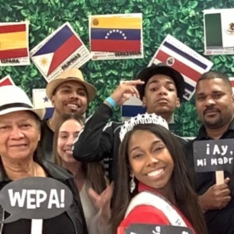 Group of friends celebrating with Puerto Rican slang photo props, Wepa and Ay Mi Madre signs at a Latin party