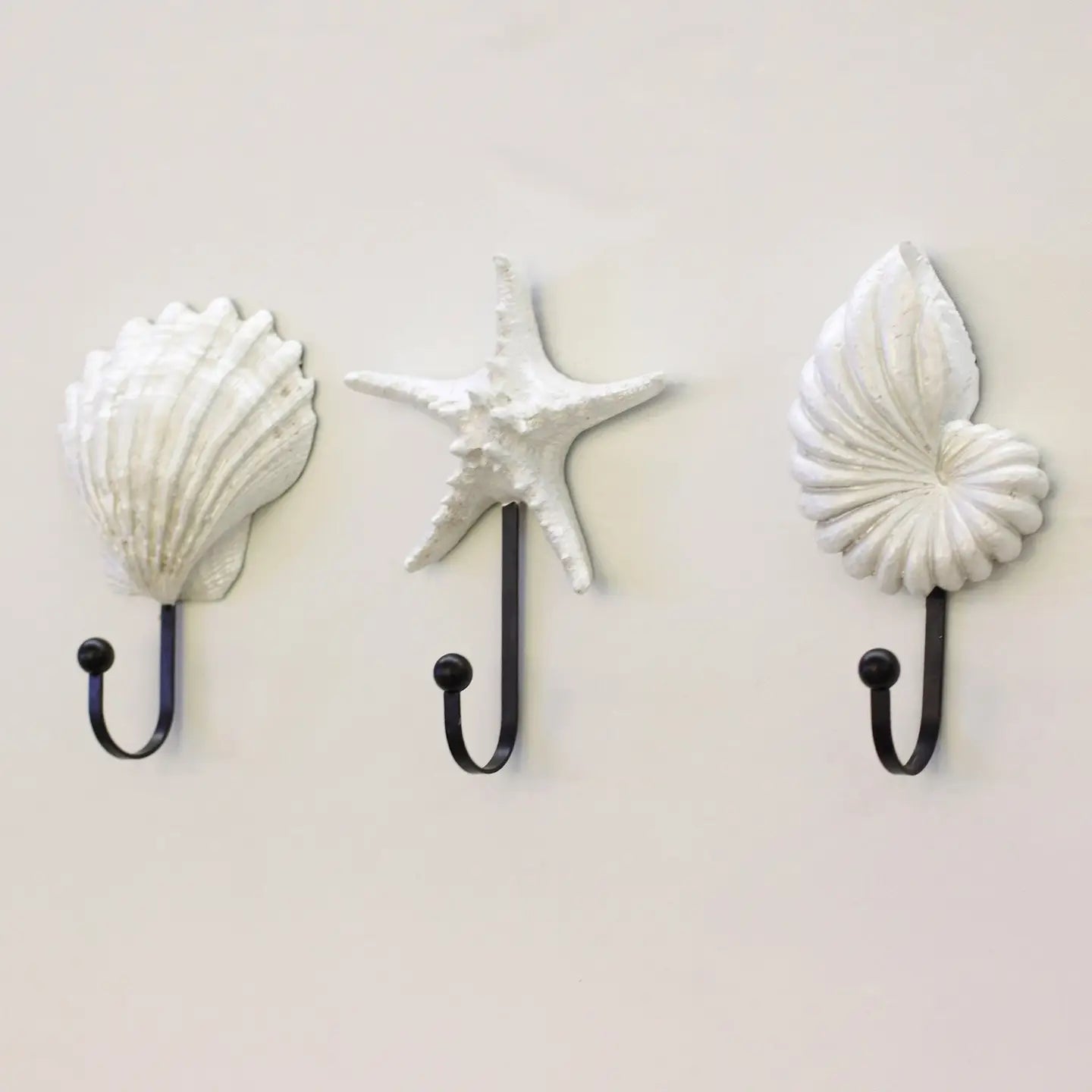 Three wall hooks shaped like shells and a starfish on a light gray background