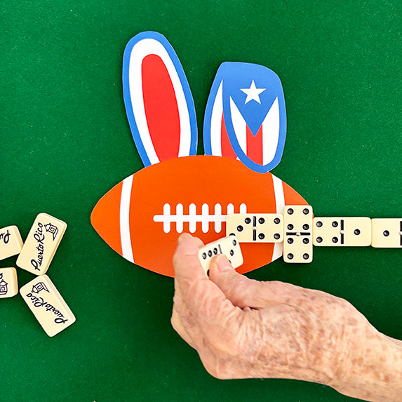 Hand playing with dominos shaped like a football and Puerto Rican flag on a green background