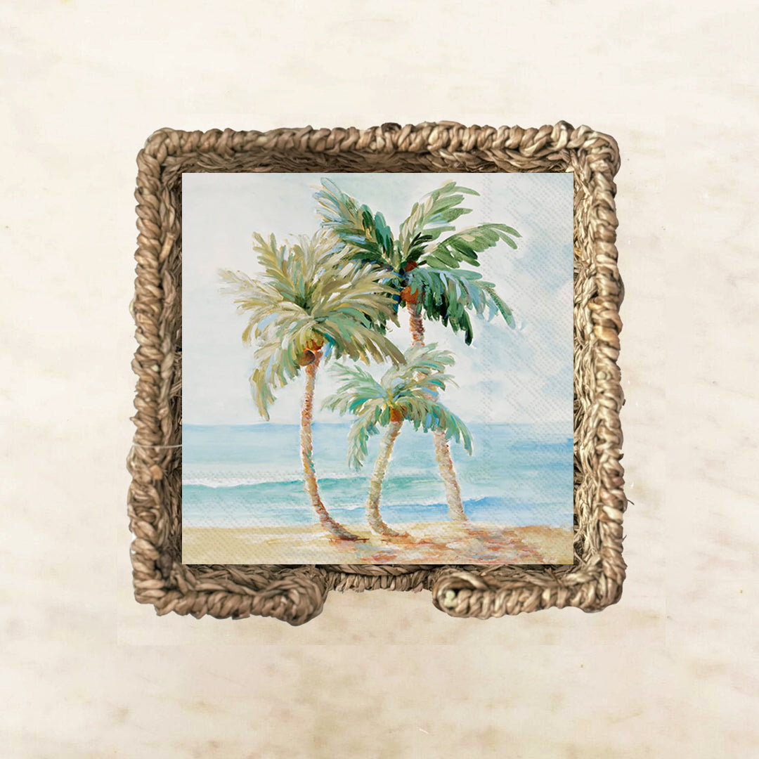 Tropical-themed cocktail napkin featuring three palm trees swaying by the ocean with blue waves and a sandy beach, perfect for coastal parties or summer entertaining.

