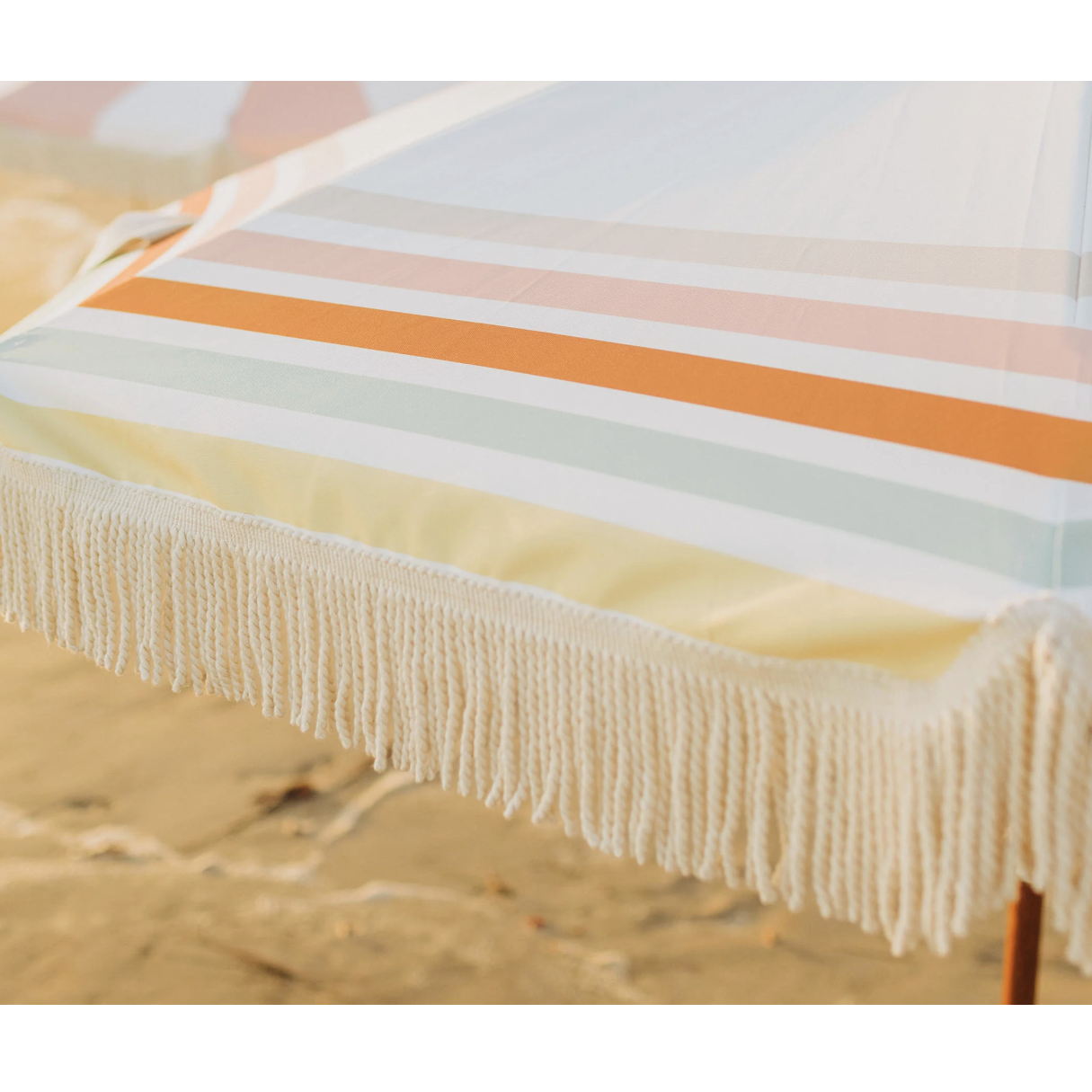 Summerland beach umbrella cotton fringe detail close-up, multicolor stripe canvas with faux wood steel pole on sandy beach