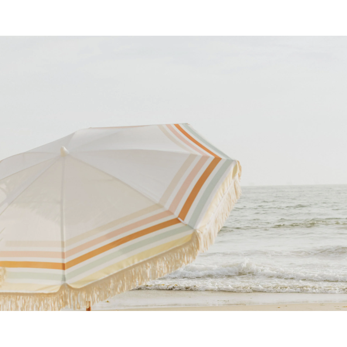 Summerland 6.5 ft beach umbrella with cotton fringe and multicolor stripes at ocean's edge, portable UV 50+ shade umbrella