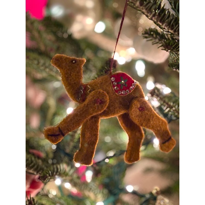 Felt camel ornament hanging on a Christmas tree with blurred lights in the background